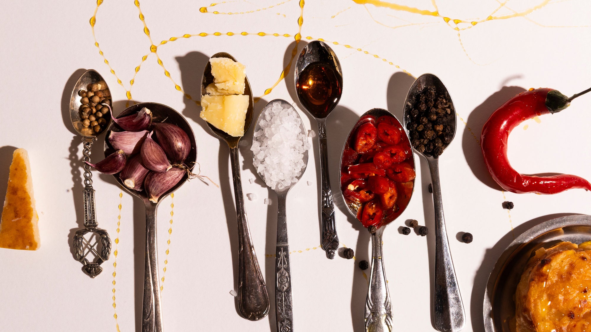 Silver spoons with various spices and ingredients on a white background showing the flavours in potato utopias gratin